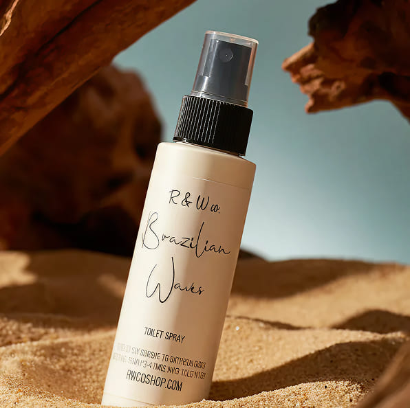 Spray bottle labeled 'R&W Brazilian Waves' on sand with natural background